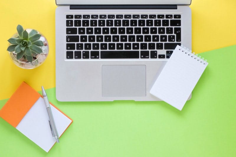 Ordinateur portable et bloc-notes sur fond coloré, symbolisant la simplicité et l'efficacité d'un site web