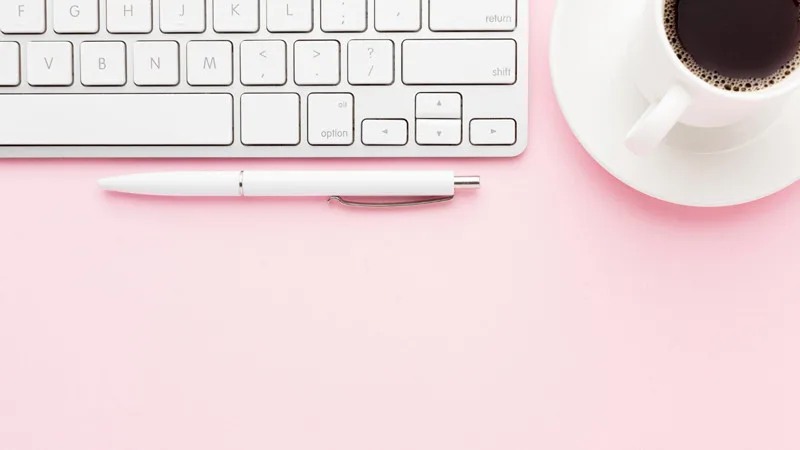 Clavier blanc, stylo et café sur fond rose – Illustration pour un article sur les meilleurs thèmes WordPress gratuits en 2025.