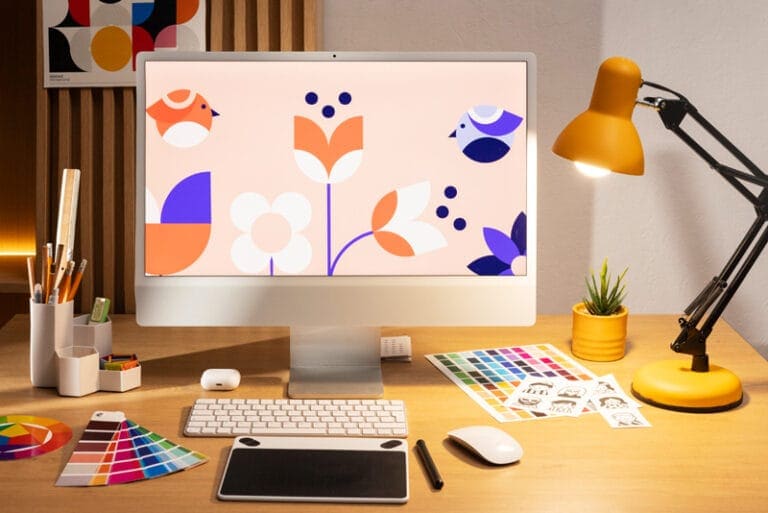 Bureau de travail avec un écran affichant un design coloré, une tablette graphique et une palette de couleurs.