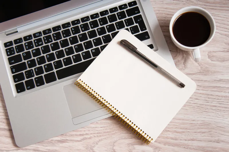 Guide pour débutants sur l’hébergement web et les noms de domaine - ordinateur, carnet et stylo pour prendre des notes.
