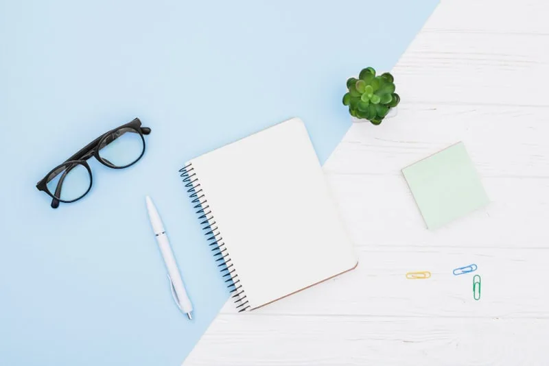 Bureau minimaliste avec carnet, lunettes et plante, représentant l'organisation et la créativité.