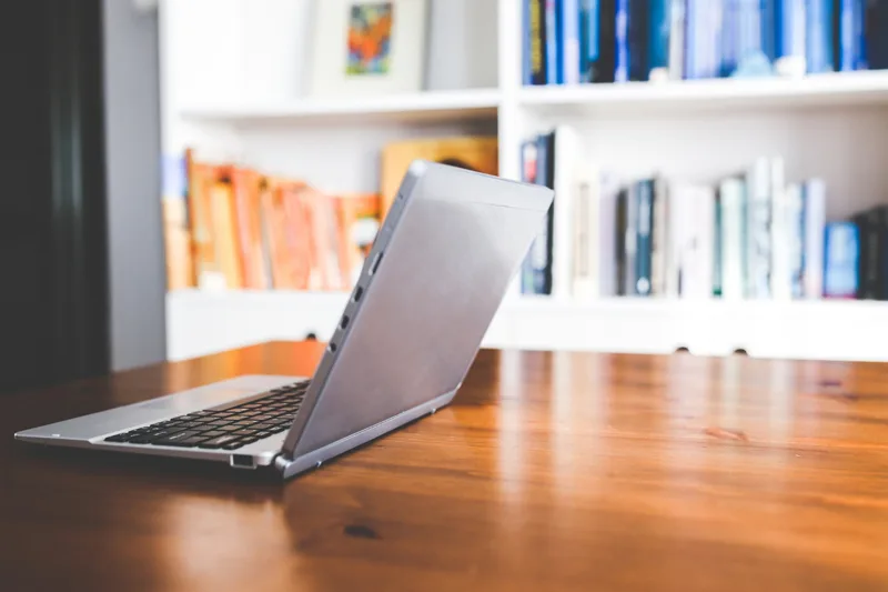 Ordinateur portable sur un bureau, avec des livres en arrière-plan, représentant la création d’une librairie en ligne pour auteurs.