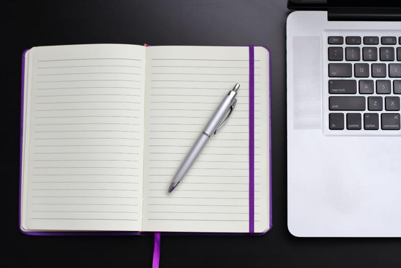 Carnet de notes avec stylo posé à côté d’un ordinateur portable, sur un fond noir