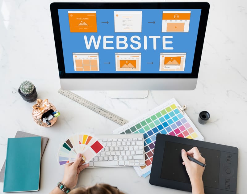 Personne créant l'identité visuelle d'un site web avec une palette de couleurs, un écran de maquette et une tablette graphique.