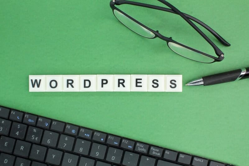 Mot WordPress écrit avec des lettres sur un bureau avec clavier, lunettes et stylo