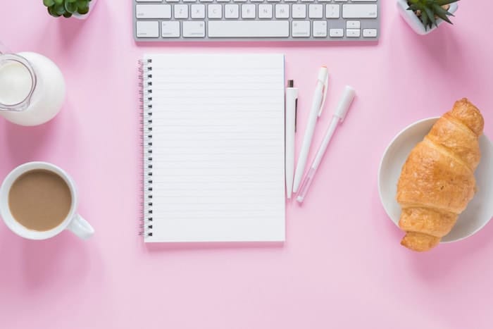 Carnet et ordinateur sur un bureau rose pastel pour illustrer la recherche d’idées d’articles de blog lifestyle