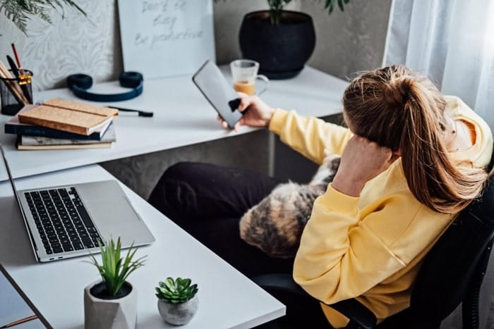Blogueuse assise à son bureau regardant son téléphone pendant une panne d’inspiration pour écrire un article de blog lifestyle