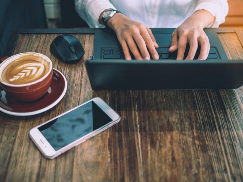 personne en train d'écrire un email sur ordinateur avec café