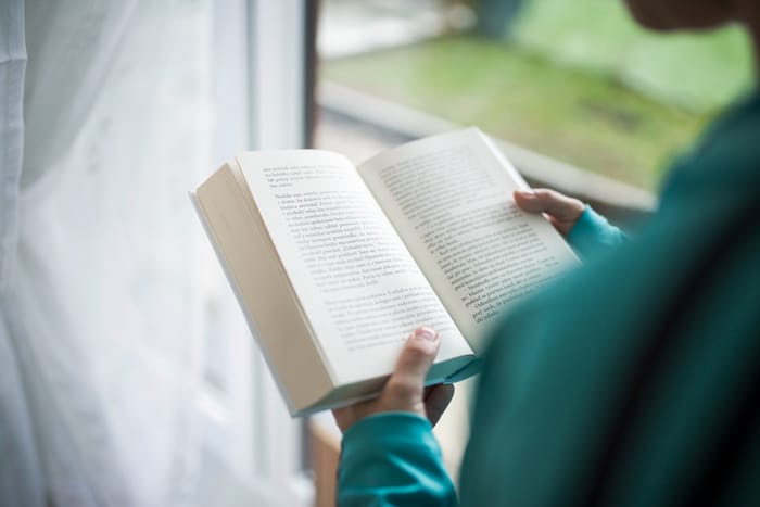 Personne lisant un livre près d’une fenêtre