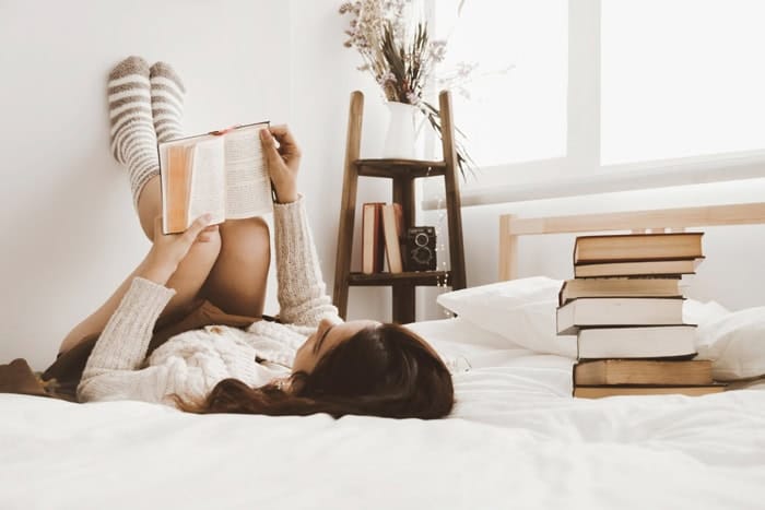 Lectrice allongée sur un lit avec plusieurs livres à ses côtés