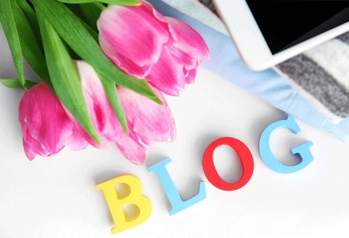 Lettres colorées formant le mot blog posées à côté de tulipes roses sur un bureau blanc
