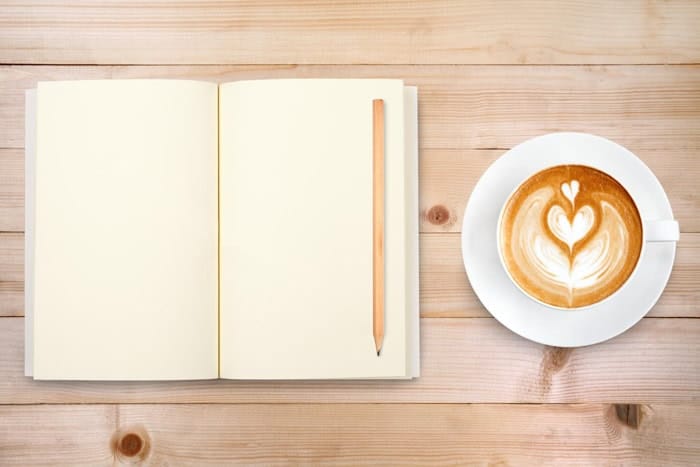 Carnet ouvert avec un crayon posé à côté d'une tasse de café sur une table en bois clair