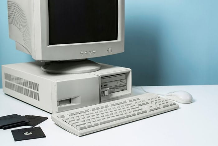 Vieil ordinateur beige avec clavier, souris et disquettes sur fond bleu clair, ambiance années 2000